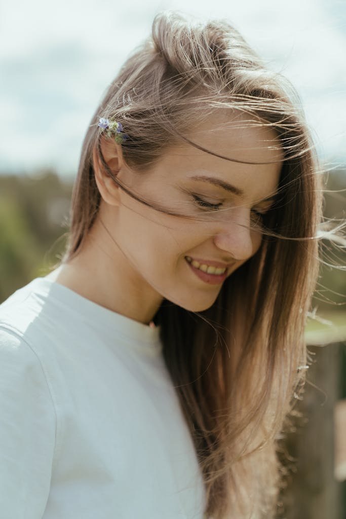 Portrait of a young woman smiling with wind in her hair, outdoors in a rural summer setting.